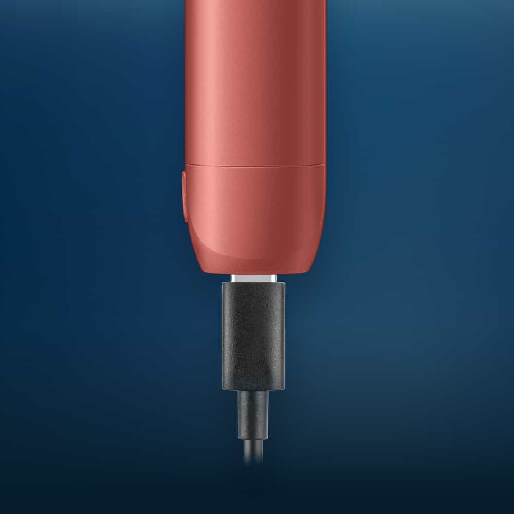 Vuse | Gros plan sur un appareil électronique rouge, probablement une brosse à dents électrique, en train de se recharger à l'aide d'un câble de recharge noir, sur fond bleu. | Cigarettes Electroniques et Recharges