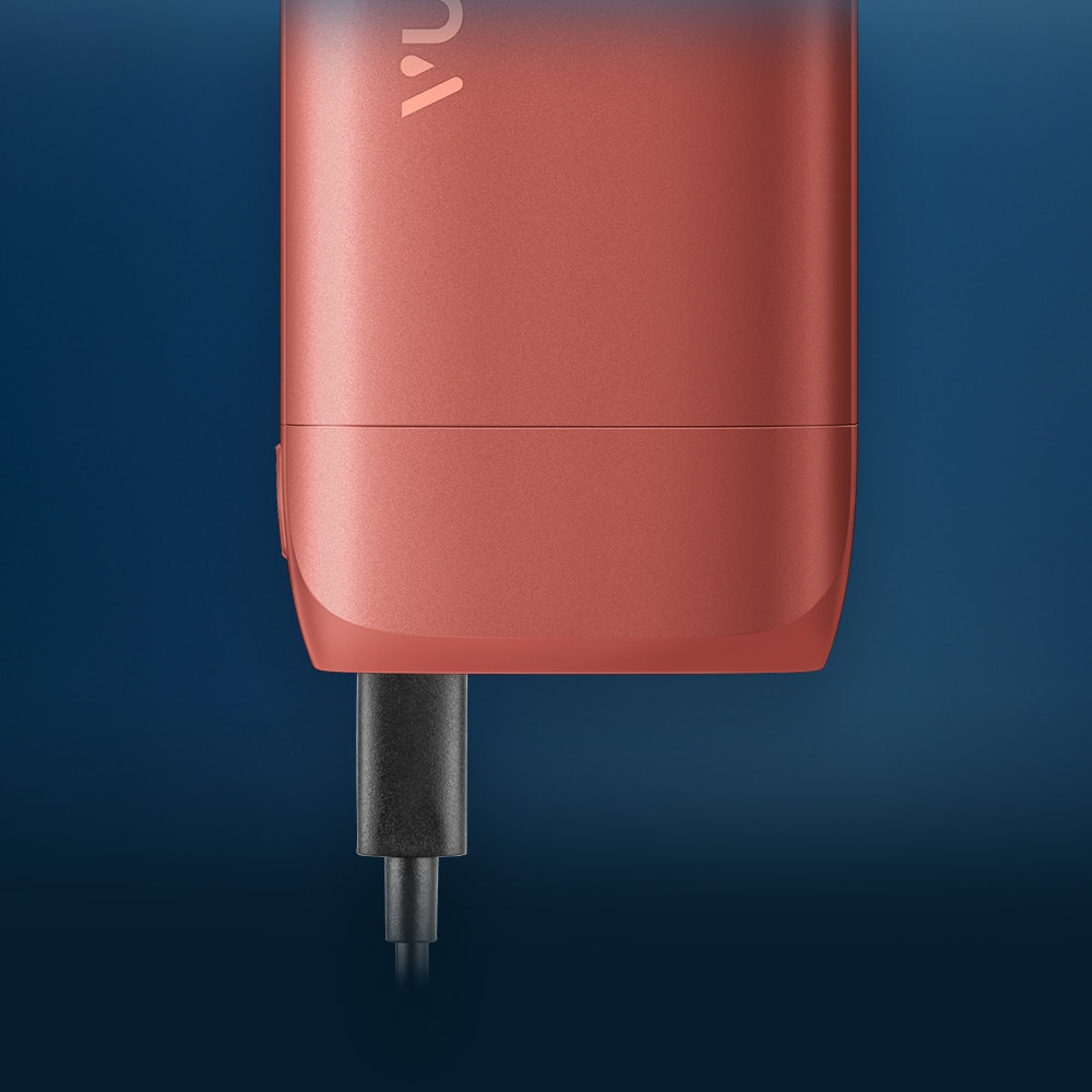 Vuse | Gros plan sur un appareil électronique rouge, avec un câble de recharge noir branché à sa base, sur fond bleu foncé. | Cigarettes Electroniques et Recharges